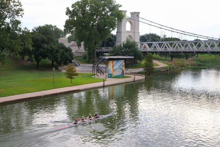 A rowing team practices on a river near a suspension bridge in McLennan County, Texas.