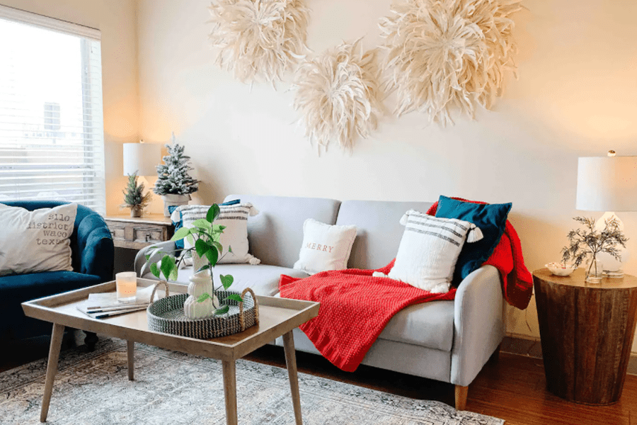 A cozy living room decorated for Christmas with a grey sofa and red throw blanket in McLennan County, Texas.