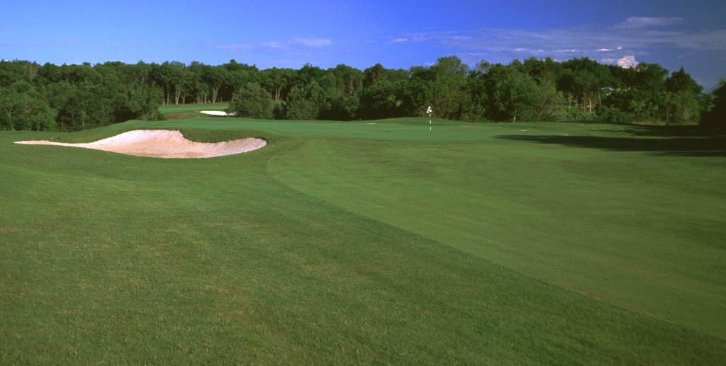 A lush green golf course hole with a sand bunker and trees in background in McLennan County, Texas.
