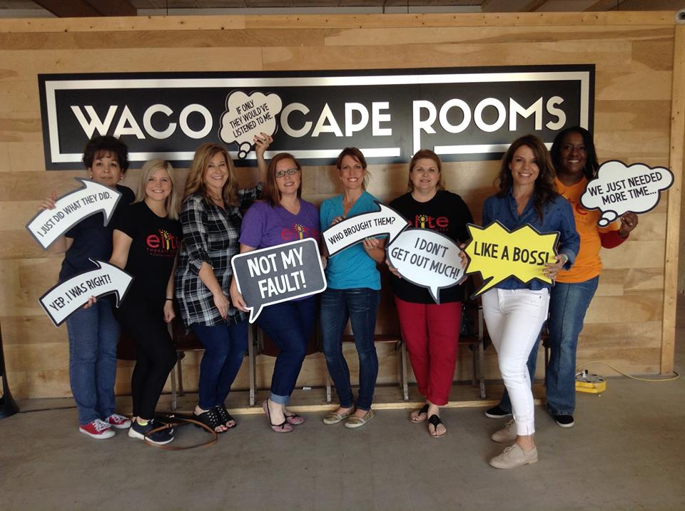 A group of eight women posing with funny speech bubble signs at an escape room in McLennan County, Texas.