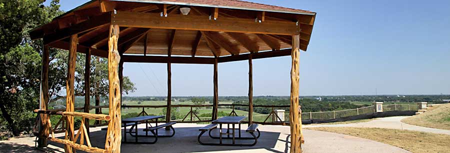 A wooden gazebo with picnic tables overlooking a vast green landscape in McLennan County, Texas.