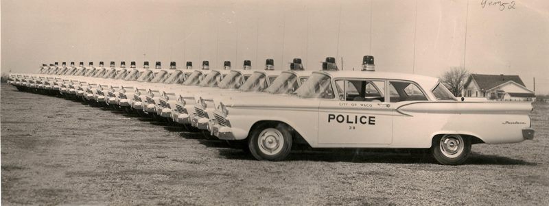 A long line of vintage Waco police cars parked in a field in McLennan County, Texas.