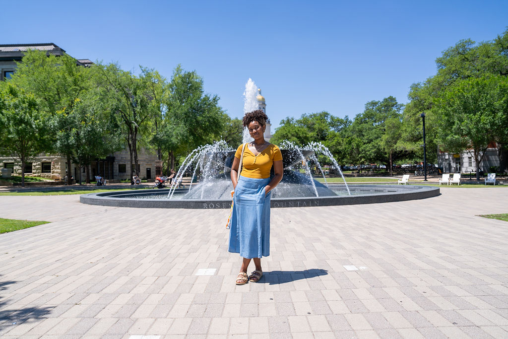 A woman stands in front of a large fountain in a sunny park in McLennan County, Texas.
