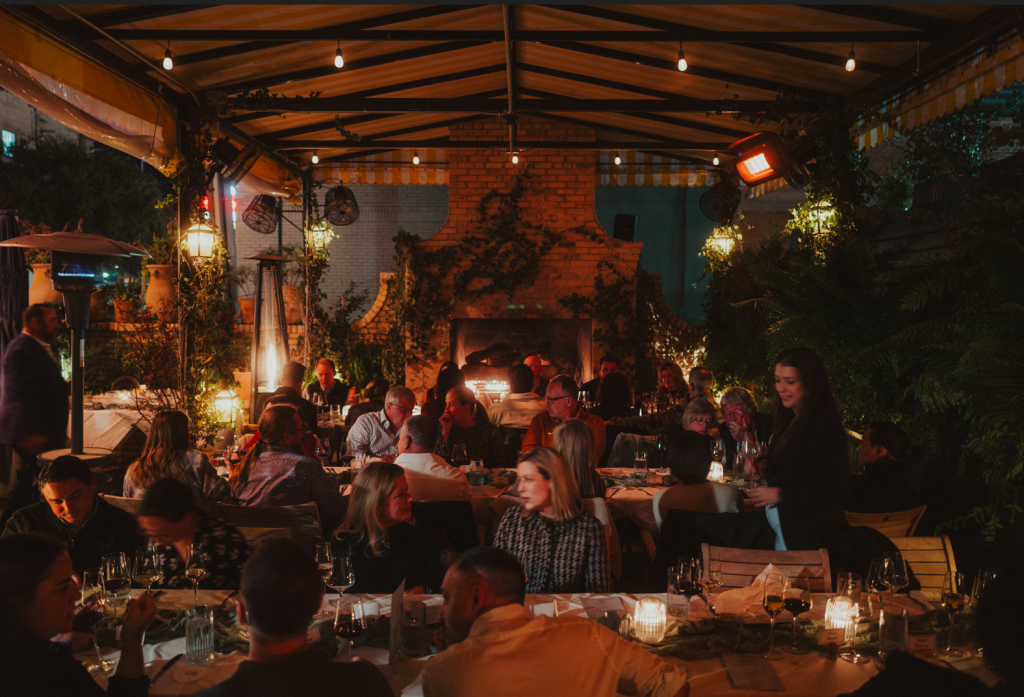 People dining at a cozy, dimly lit outdoor restaurant patio with a brick fireplace in McLennan County, Texas.