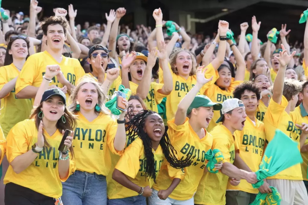 A large crowd of excited students wearing yellow Baylor shirts cheering at a game in McLennan County, Texas.