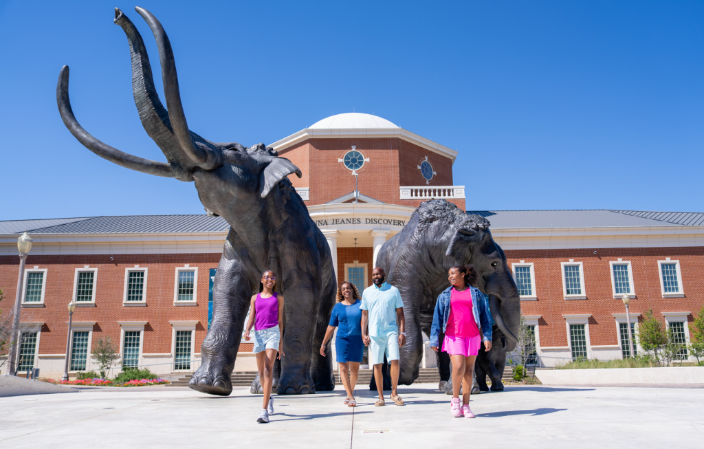 A family walks in front of two large mammoth statues outside a brick building in McLennan County, Texas.