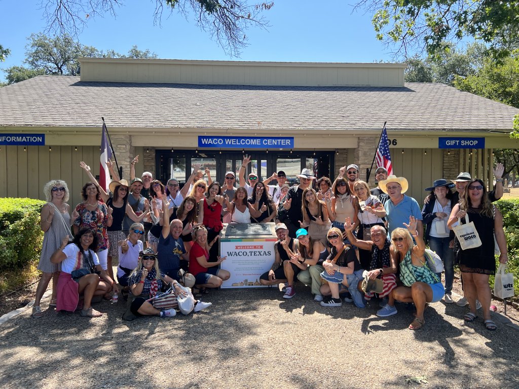A large group of people posing in front of the Waco Welcome Center in McLennan County, Texas.