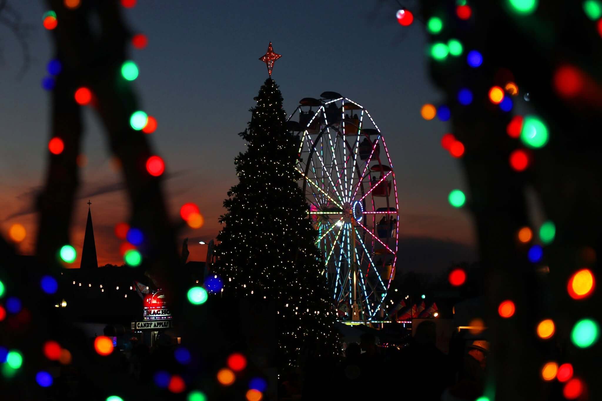 A lit Christmas tree and a ferris wheel at a carnival during twilight in McLennan County, Texas.