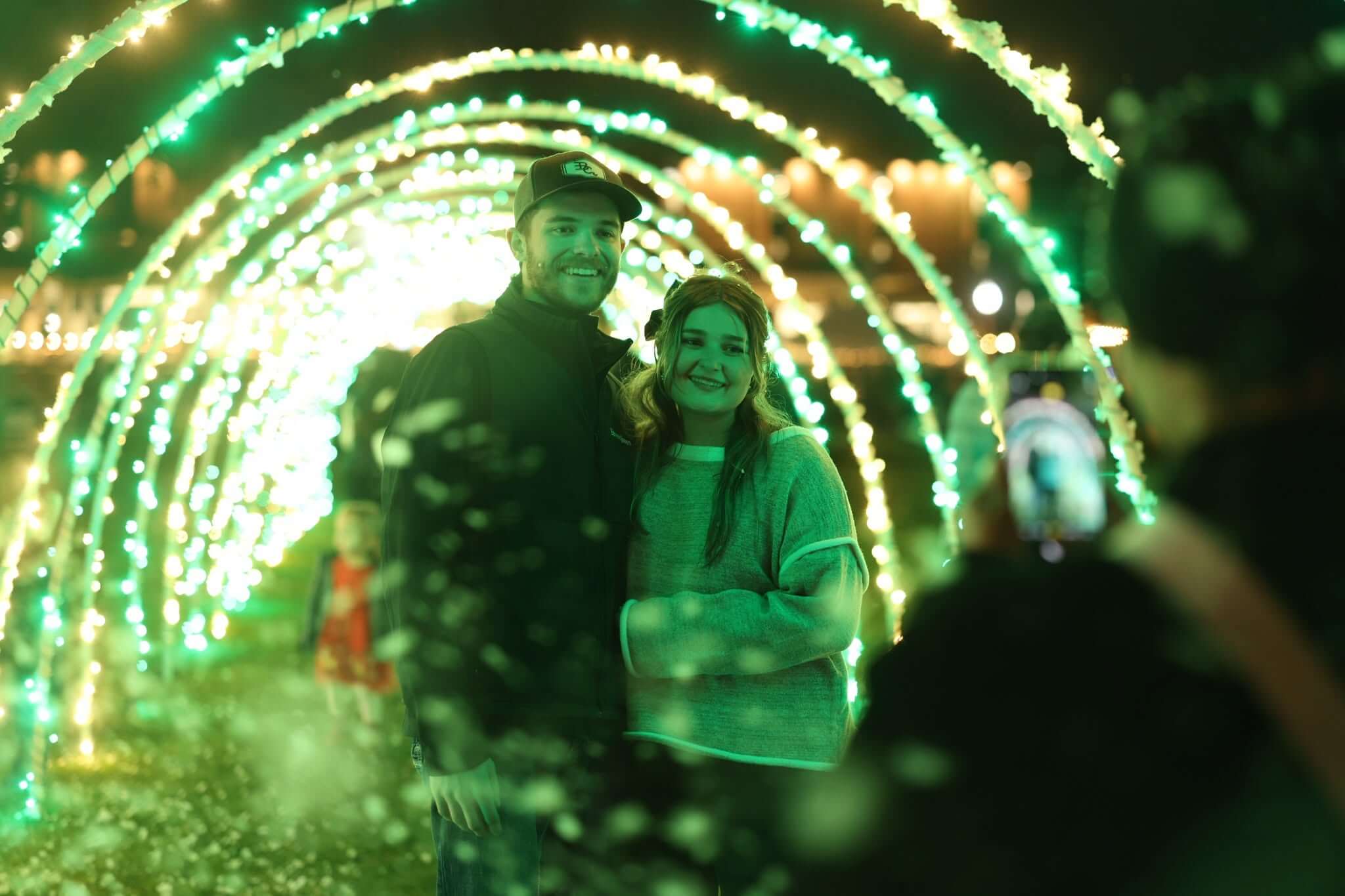 A smiling couple posing for a photo inside a tunnel of glowing green lights in McLennan County, Texas.