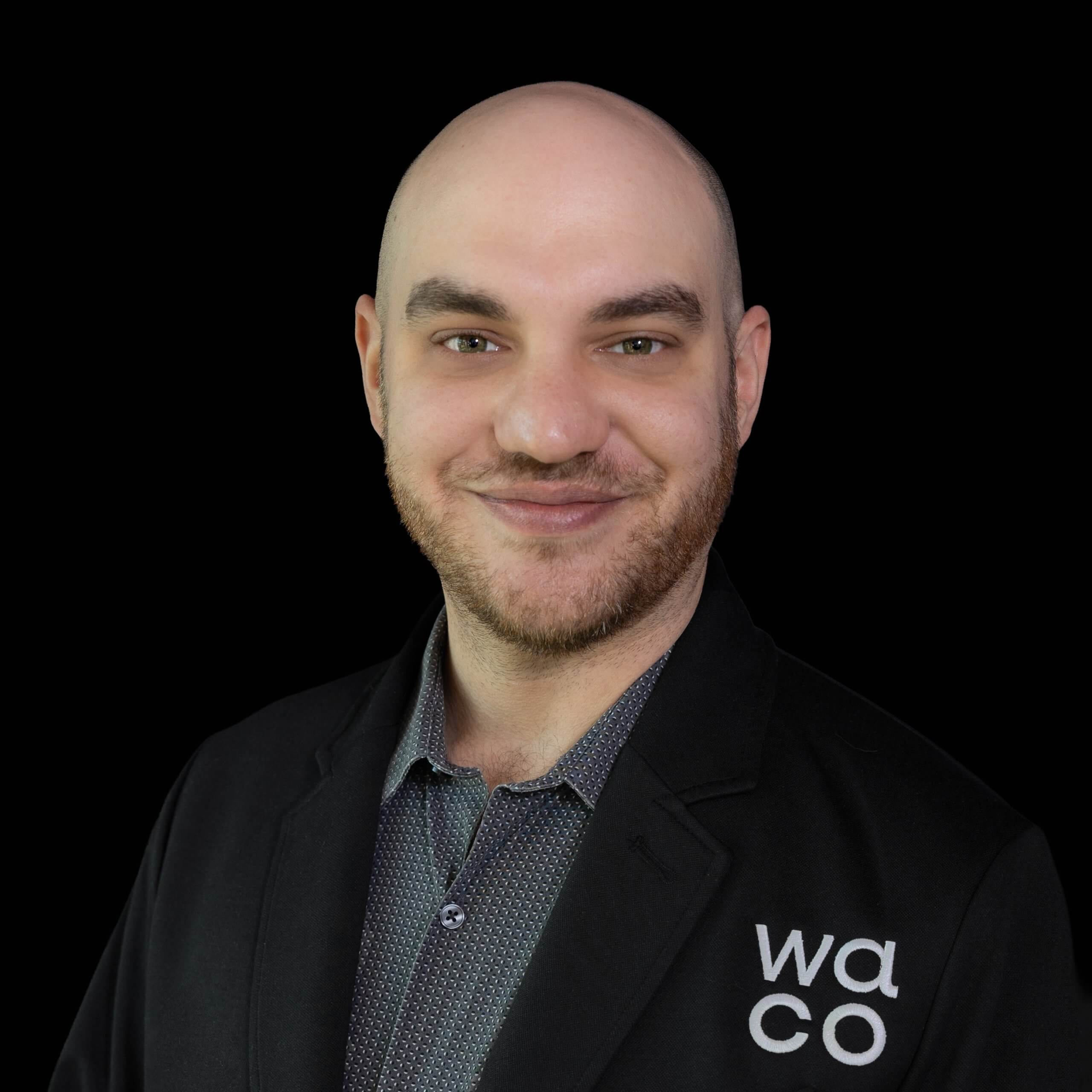 A bald man with a beard wearing a black blazer smiles against a black background in McLennan County, Texas.