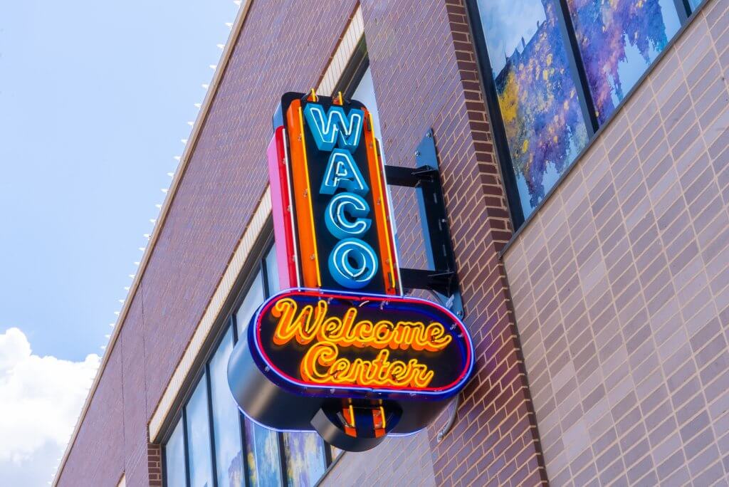 A bright neon sign for the Waco Welcome Center mounted on a brick building in McLennan County, Texas.