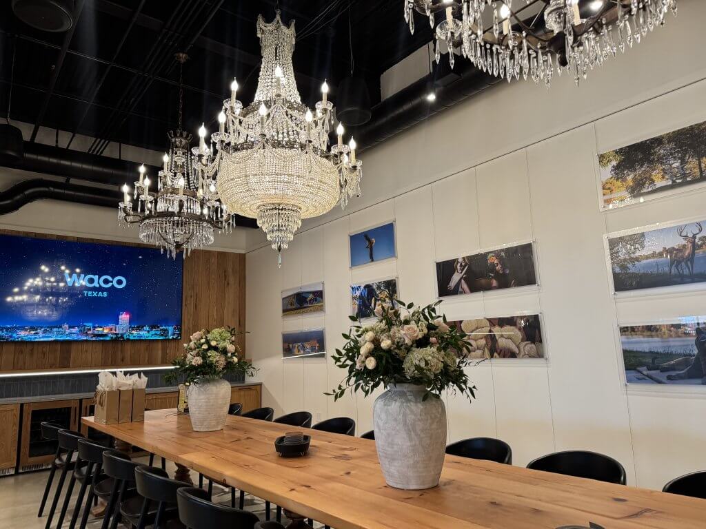A long wooden table with floral arrangements sits beneath ornate crystal chandeliers in a room in McLennan County, Texas.