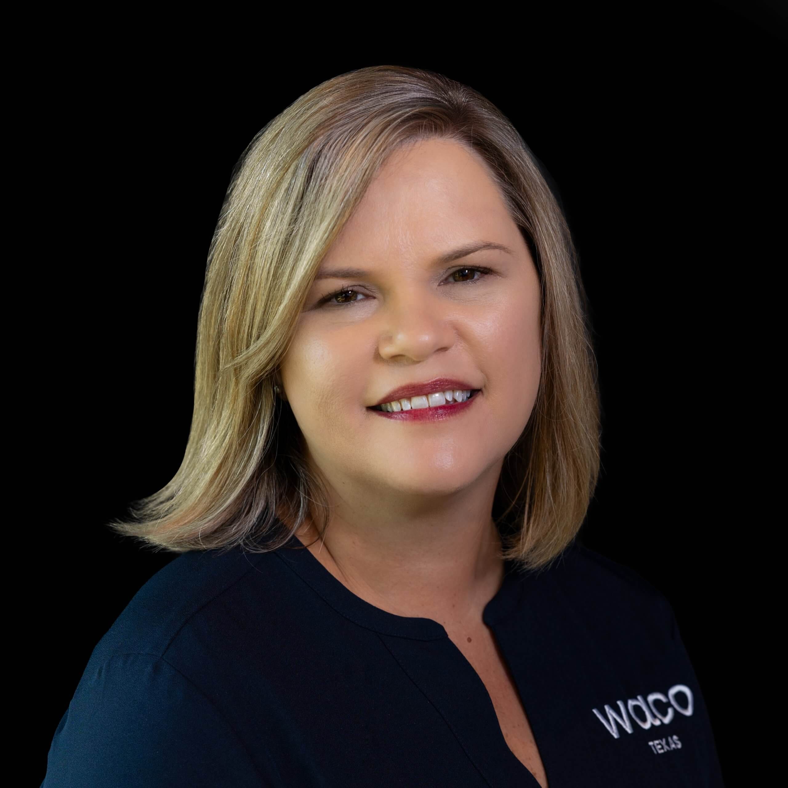 A professional headshot of a smiling woman with blonde hair against a black background in McLennan County, Texas.