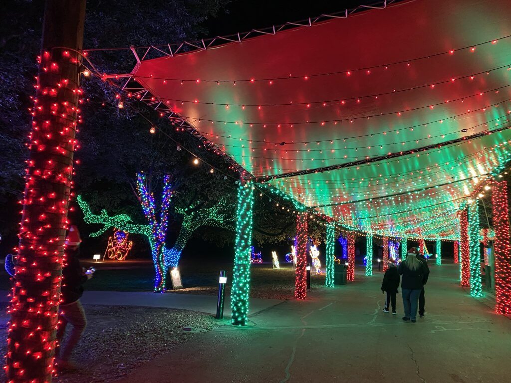 People walking under a canopy decorated with festive red and green Christmas lights at night in McLennan County, Texas.