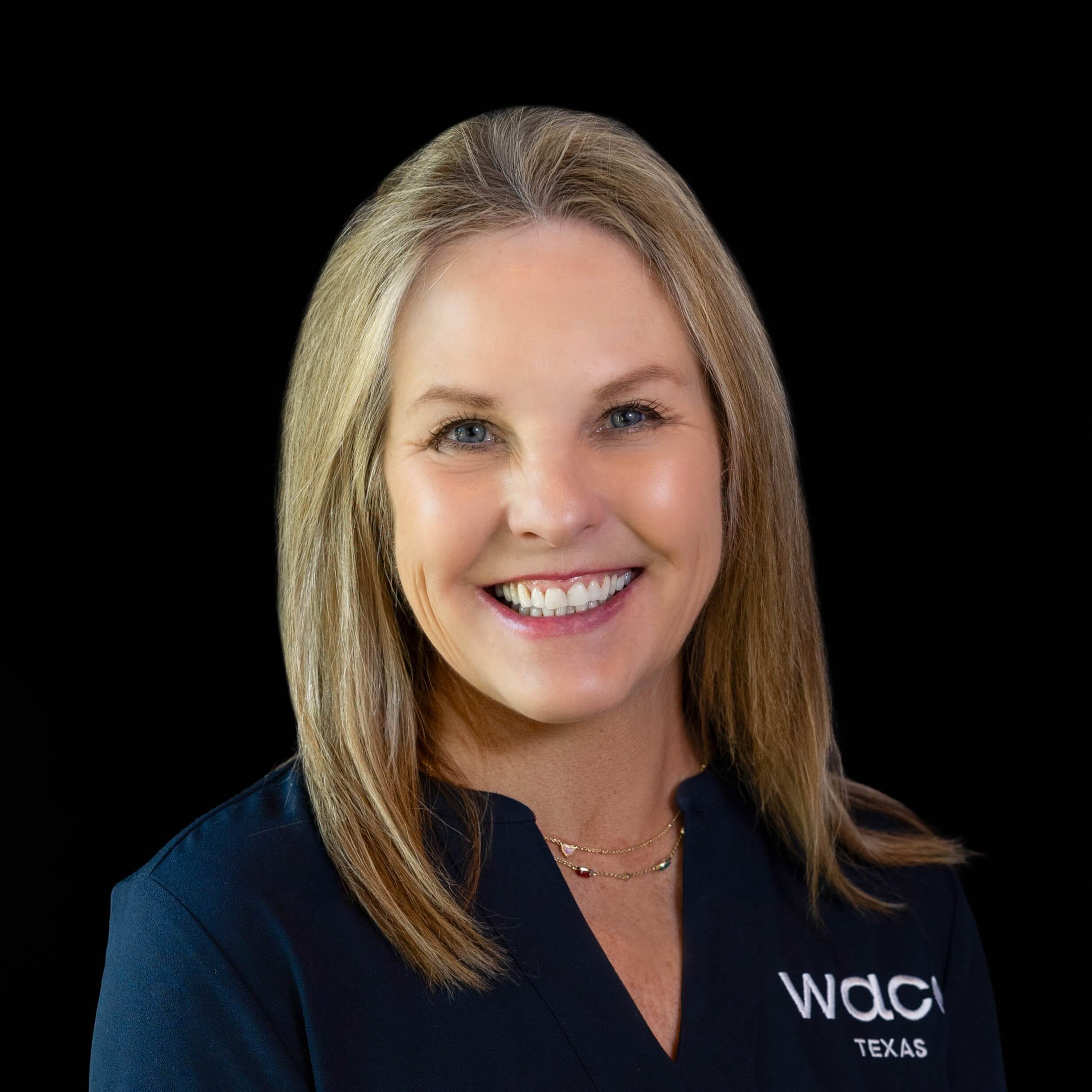 A smiling woman with blonde hair wearing a dark blue top against black background in McLennan County, Texas.