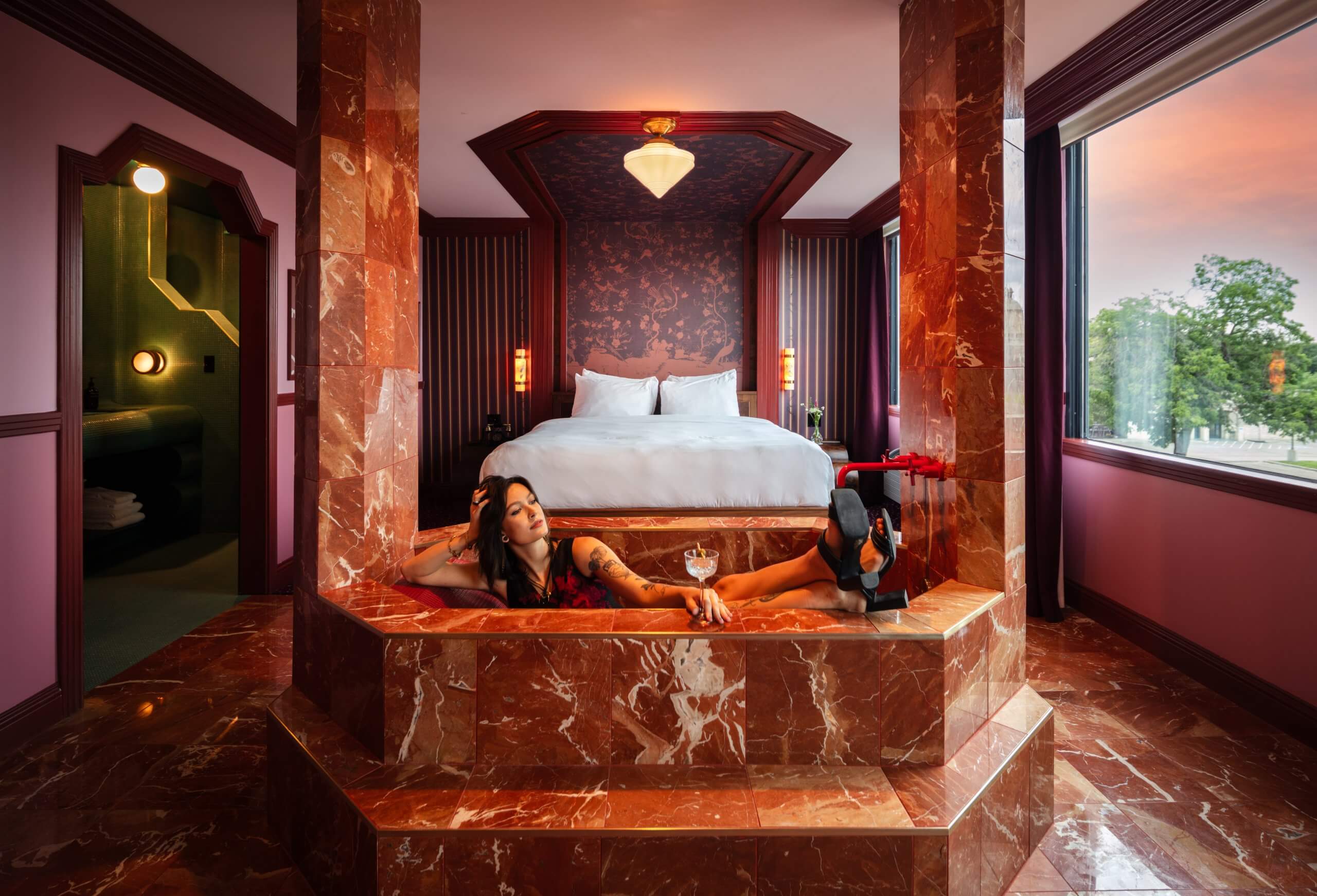 A woman relaxes in a red marble bathtub inside a luxurious hotel room in McLennan County, Texas.