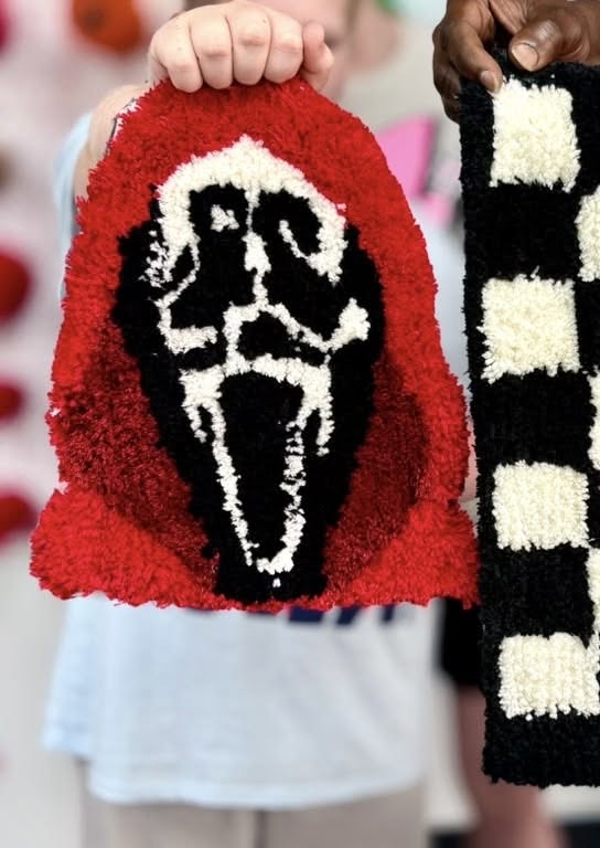 Hands holding a handmade tufted rug featuring the Scream ghostface mask design in McLennan County, Texas.