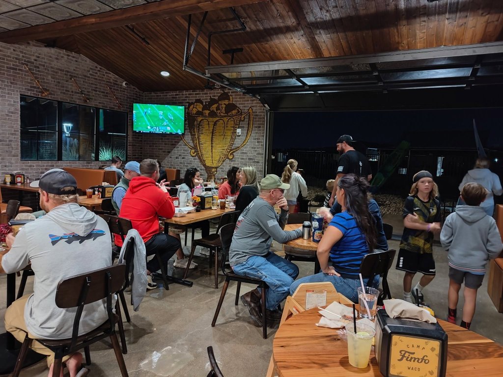 People dining and socializing in a rustic, open-air restaurant with a large mural in McLennan County, Texas.