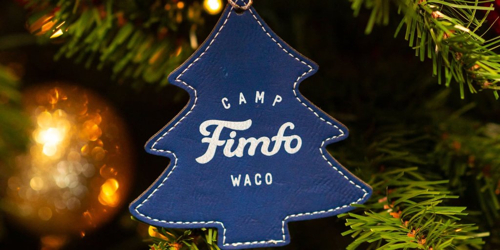 A blue leather Christmas tree ornament labeled Camp Fimfo Waco hanging on a tree in McLennan County, Texas.