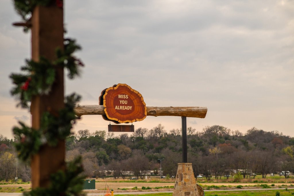 A wooden sign shaped like a tree slice reads Miss You Already in McLennan County, Texas.