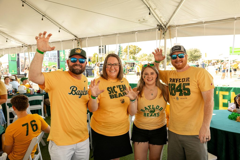 Four people wearing Baylor University gear pose with bear claw hand gestures in McLennan County, Texas.