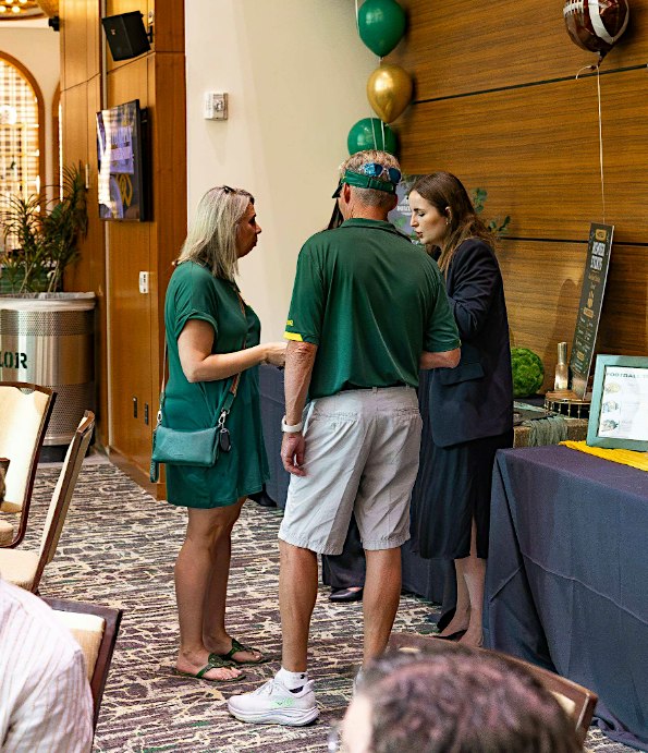 Three people standing and talking in a room decorated with green and gold balloons in McLennan County, Texas.