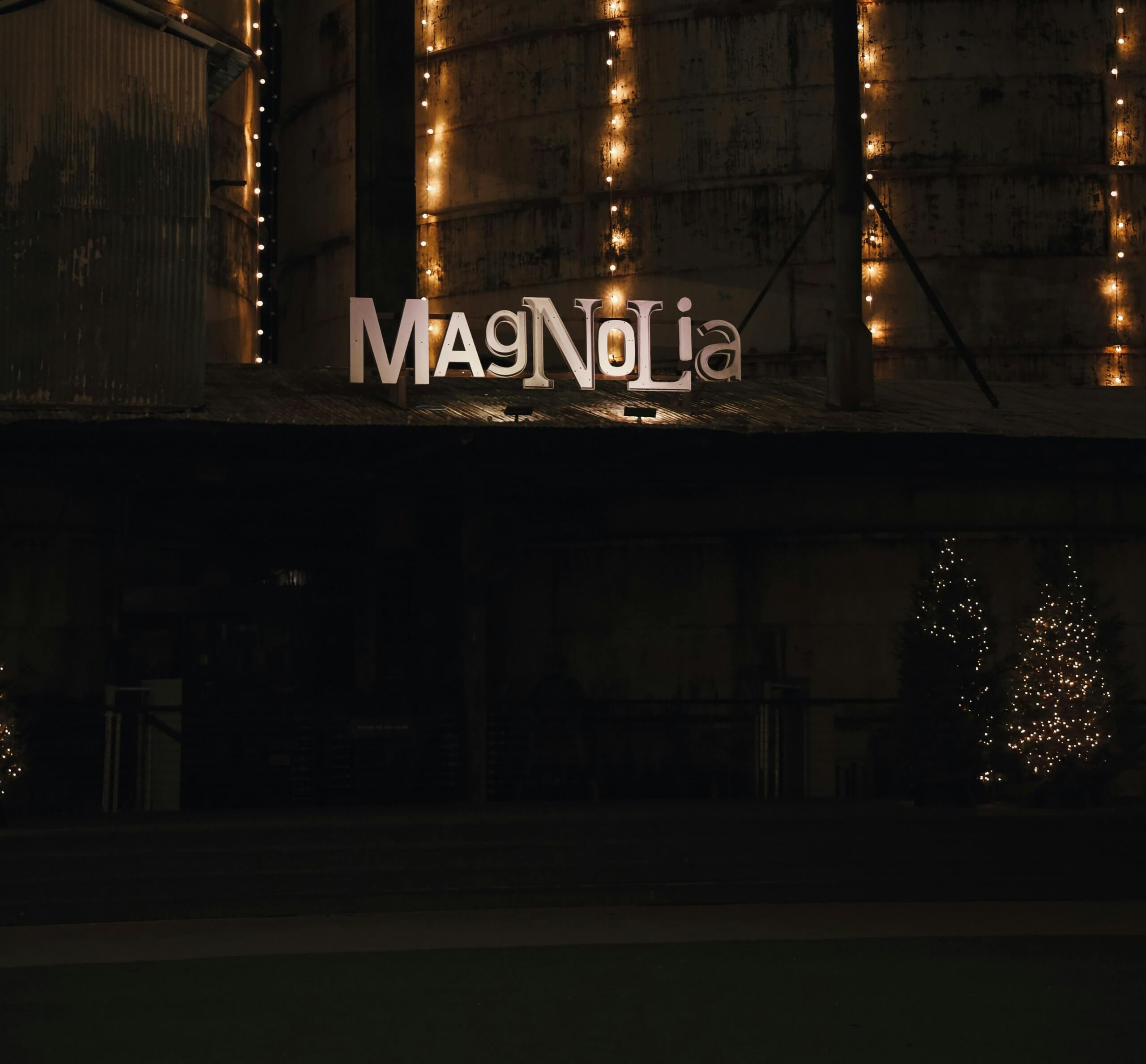 The Magnolia sign illuminated at night against industrial silos decorated with string lights in McLennan County, Texas.